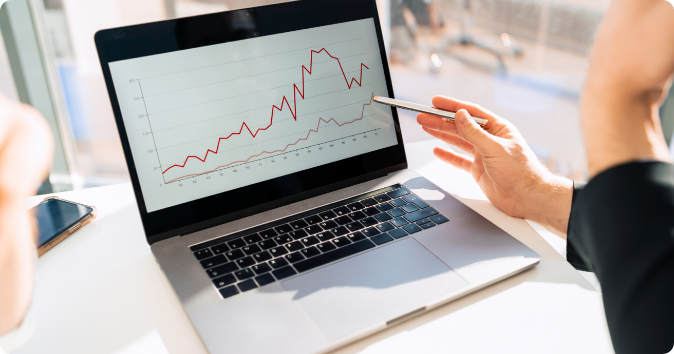 A person uses a pen to point to a graph on a laptop computer